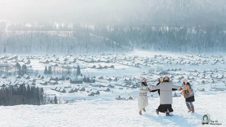 几个人走在雪坡上，远处是白雪覆盖的村落与山林